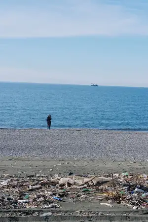 Одинокая фигура на загрязненном побережье, окруженная мусором и отходами, иллюстрирующая экологическую проблему и необходимость уборки на берегу моря