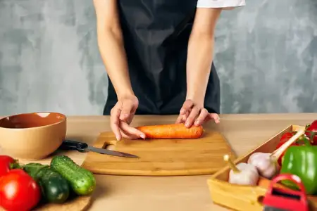 Женщина-повар на кухне нарезает овощи на разделочной доске