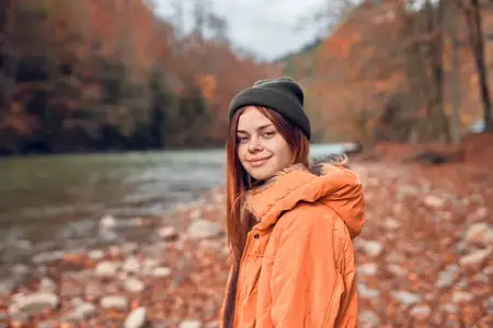 Симпатичная женщина в осенней одежде в лесу у реки среди опавших листьев