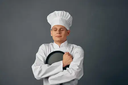 Повар-мужчина держит в руке сковороду, работая на кухне ресторана и занимаясь приготовлением пищи