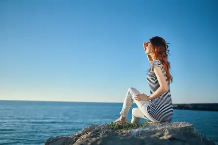 Женщина на пляже в горах, вид сверху: синее море и облака