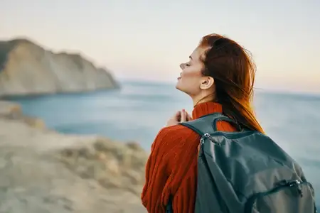 Женщина путешествует с рюкзаком рядом с морем в горах на природе