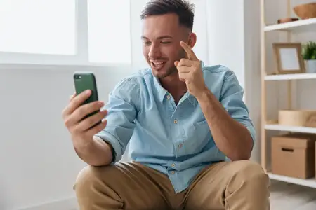 Весёлый, улыбчивый, общительный парень разговаривает с семьёй по видеозвонку, обсуждает последние приятные новости, поднимает палец вверх и смотрит на экран