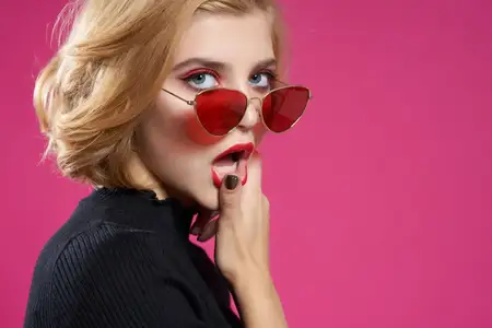 Гламурная блондинка в солнцезащитных очках, крупный план, розовый фон, красные губы