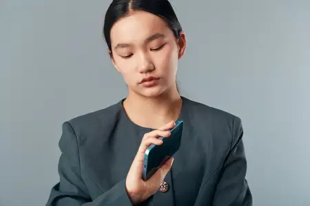 Деловая женщина держит смартфон в темно-серой одежде с сосредоточенным выражением лица