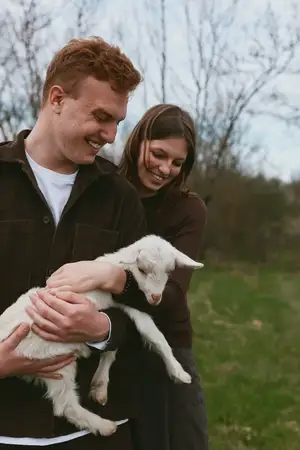 Повседневная сцена показывает любящую пару с ягнёнком на улице, демонстрируя деревенскую жизнь, тепло и привязанность к животным на ярком поле, подходящем для тем образа жизни и семьи