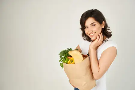 Женщина в белой футболке держит пакет с полезными продуктами — овощами