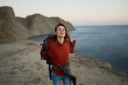 Женщина на фоне осеннего пейзажа: горы, море, пляж, рюкзак