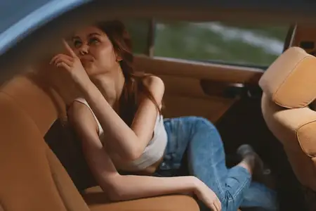 Игривая молодая женщина отдыхает внутри автомобиля, одетая в повседневную одежду и демонстрируя расслабленное выражение лица, что подчёркивает моменты спонтанности и приключений в лайфстайл-фотографии