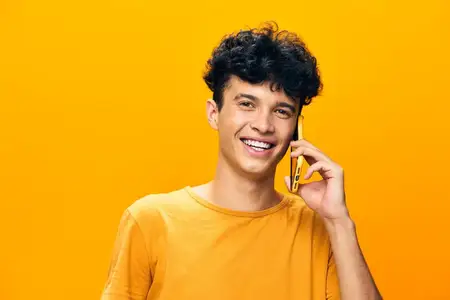 Молодой человек улыбается и разговаривает по смартфону на ярко-жёлтом фоне