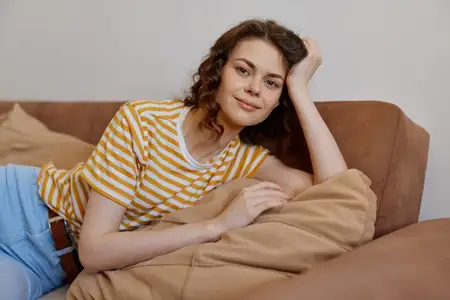 Непринуждённый домашний портрет женщины, отдыхающей на диване с подушками, подчёркивающий комфорт, расслабление и уютные повседневные моменты в уютной гостиной