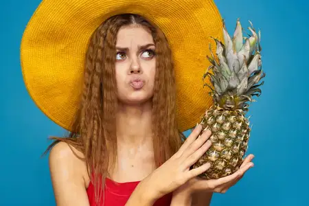 Женщина в жёлтой шляпе держит в руках ананас, передавая эмоции и веселье