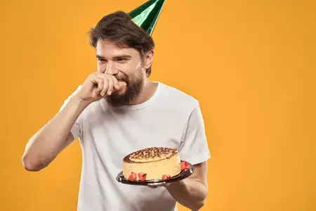 Именинник в кепке с тортом веселится на вечеринке на жёлтом фоне