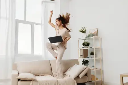 Улыбающаяся женщина использует ноутбук, печатает и работает из дома в уютной гостиной