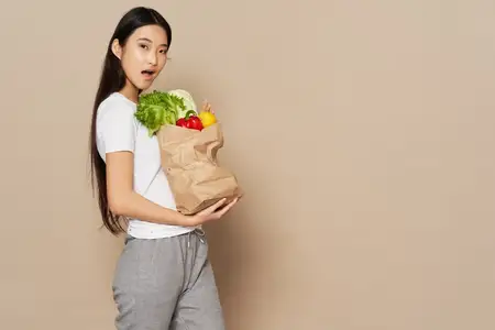 Симпатичная женщина в спортивных штанах и футболке держит в руках пакет с продуктами