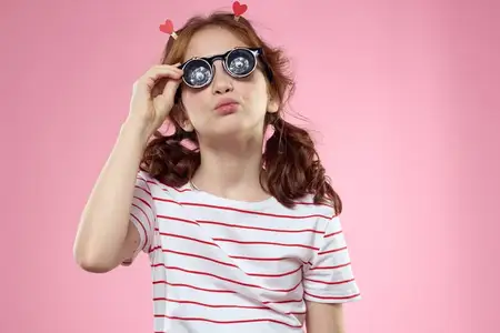 Счастливая девочка с кудрявыми волосами и в очках, одетая в полосатую футболку
