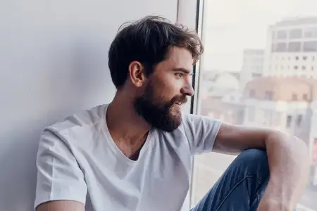 Мужчина в белой футболке сидит на подоконнике в наушниках, общение