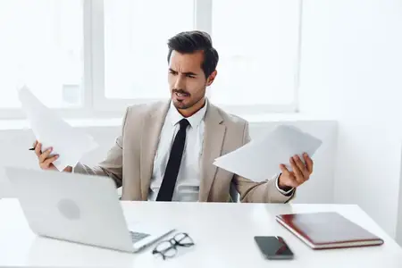 Улыбающийся мужчина в деловом костюме держит документ и работает за ноутбуком