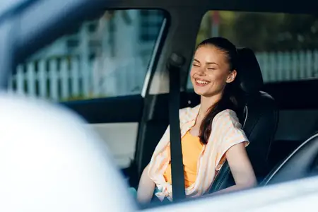 Весёлая девушка сидит в автомобиле, наслаждаясь солнечным днём