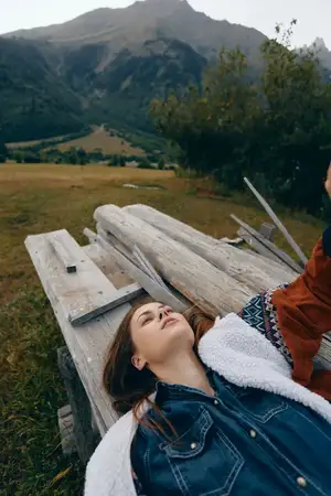 Женщина отдыхает, полулежа на деревянной скамье в горах, на лугу