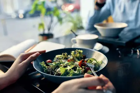 Вкусная еда: салат на тарелке, вилка, блокнот с надписью и женщина в рубашке в интерьере кафе