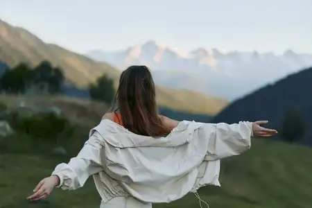 Одинокая женщина в легкой куртке наслаждается открытым пейзажем, потягиваясь и вдыхая свежий воздух, создавая настроение обновления, покоя и отдыха на природе