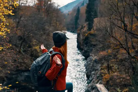 Женщина-туристка с рюкзаком у реки, горы, осенний лес, путешествие