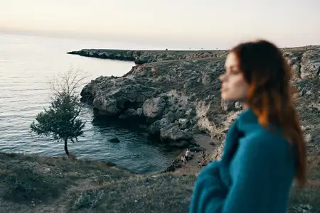 Красивая женщина в горах с пледом на плечах возле моря, модель у дерева