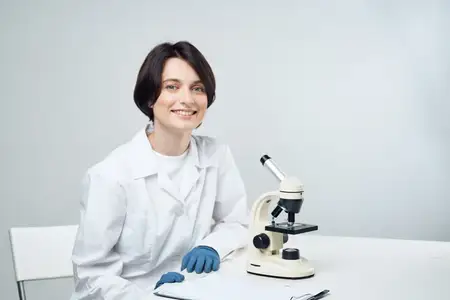 Женщина-лаборант работает с микроскопом, занимается исследованиями в области медицины и науки