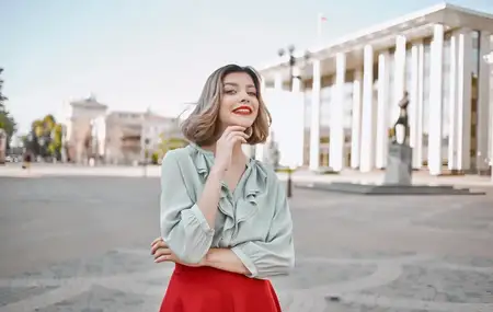 Женщина в рубашке и юбке прогуливается по центральным улицам города, на заднем плане видны высотные здания
