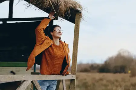 Женщина на отдыхе, портрет на открытом воздухе: улыбается в очках, опирается на деревянную платформу в сельской местности, свежий воздух, теплый солнечный свет и небо, свитер, спокойное…