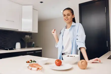 Женщина стоит на кухне с миской овощей и фруктов, готовя здоровую еду для семьи
