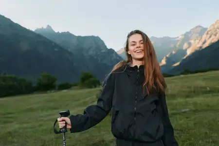 Путешественник-одиночка наслаждается отдыхом на природе в непромокаемой куртке, сохраняя устойчивую стойку и излучая энергию во время исследования живописной долины