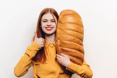 Красивая женщина в желтой рубашке держит в руке большой каравай