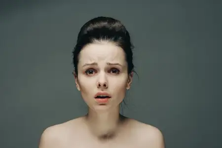 Испуганное лицо женщины с обнаженными плечами, прическа, серый фон, модель
