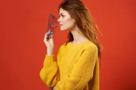 Симпатичная женщина в желтом свитере и очках, привлекательный взгляд, обрезанный вид, красный фон