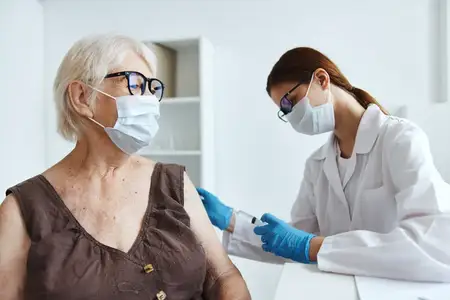 Медсестра в белом халате делает пациенту инъекцию вакцины, рядом лежит паспорт вакцинации