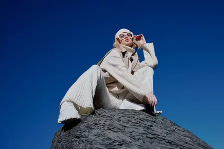 Женщина в осенней одежде стоит на скале на фоне голубого неба и пейзажа