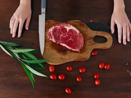 Женщина с ножом в руке нарезает свежее мясо стейка для жарки на кухне