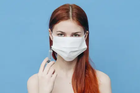 Эмоциональная женщина со шприцем в руке и медицинской маской, инъекция, вакцина на синем фоне