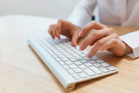 Крупный план рук бизнесвумен, журналистки, офисной работницы, фрилансерки, печатающей отчёт и работающей с документами на клавиатуре