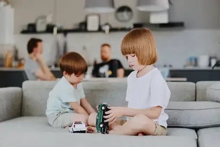Восхитительная сцена: двое мальчиков заняты воображаемой игрой с игрушечными машинками на удобном диване