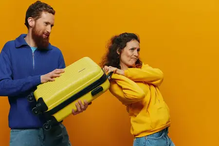 Улыбающиеся женщина и мужчина с чемоданами в руках, жёлтый и красный чемоданы, весело и криво улыбаются, жёлтый фон, собираются в путешествие, семейная поездка, молодожёны