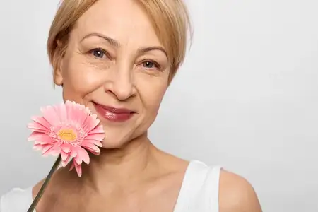 Улыбающаяся зрелая женщина, крупный план портрета, держит розовый цветок