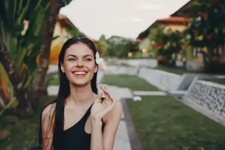 Счастливая женщина позирует на фоне здания с пальмой в солнечный день