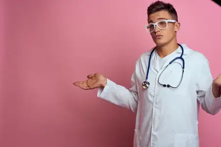 Врач-мужчина в медицинском халате со стетоскопом на шее на розовом фоне, в очках