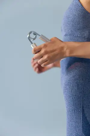 Энтузиастка спортивного фитнеса в синей спортивной одежде сжимает кистевой эспандер, демонстрируя преданность и силу во время упражнения, на мягком синем фоне