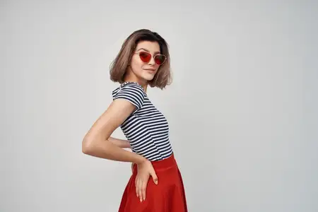 Привлекательная женщина в полосатой футболке и очках на сером фоне