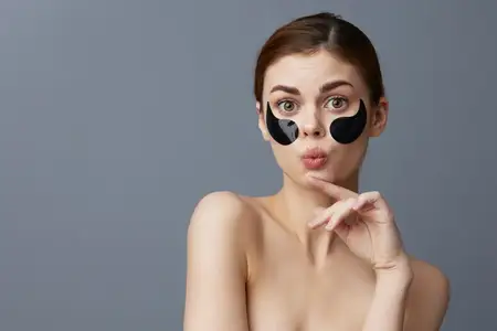 Портрет женщины с патчами для глаз на лице, обнаженными плечами и уходом за кожей на изолированном фоне