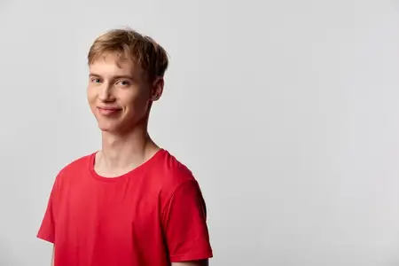 Молодой человек в повседневном стиле, одетый в красную рубашку, в минималистичной студийной обстановке с ярким освещением и нейтральным фоном, передаёт дружелюбное настроение для проектов…